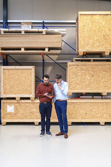 Businessman with colleague using tablet computer in front of thermal insulated containers at warehouse - JOSEF13855