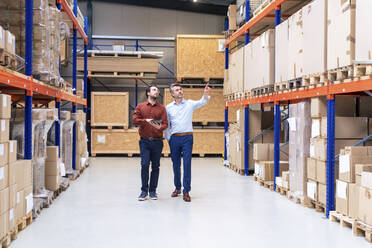 Businessman with colleague pointing at containers in warehouse - JOSEF13857