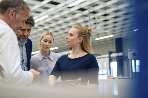 Blond businesswoman with colleagues discussing over tablet computer - JOSEF13876