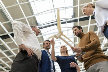 Smiling businesswoman with colleagues discussing over wind turbine model at industry - JOSEF13891