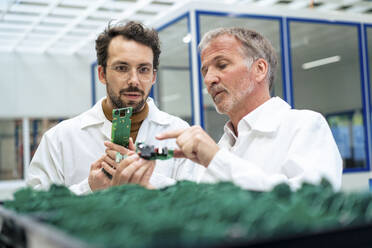 Senior engineer discussing over circuit board with colleague at industry - JOSEF13918