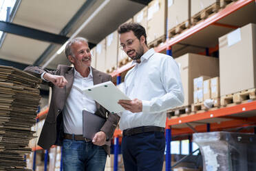 Happy senior businessman with colleague discussing over document at warehouse - JOSEF13920