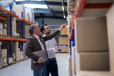 Senior businessman discussing over inventory with colleague at warehouse - JOSEF13921