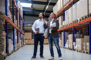 Happy senior businessman discussing over inventory with colleague at warehouse - JOSEF13924