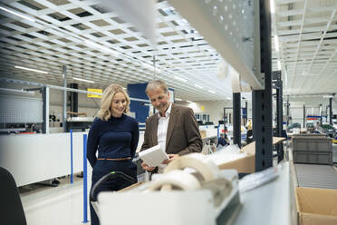 Smiling businesswoman with colleague examining machine part at industry - JOSEF13958