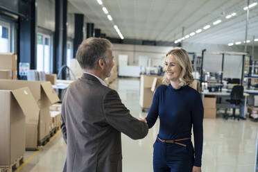 Happy businesswoman handshaking with colleague at warehouse - JOSEF13989