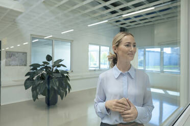 Smiling businesswoman with smart phone seen through glass - JOSEF14033