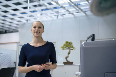 Glückliche junge Geschäftsfrau mit Mobiltelefon in der Industrie stehend - JOSEF14054