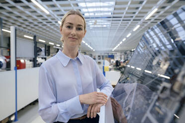 Smiling businesswoman standing by desktop computer at industry - JOSEF14058