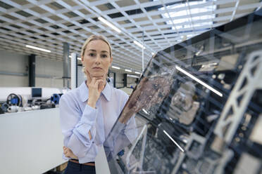 Thoughtful businesswoman with hand on chin standing by desktop computer at industry - JOSEF14060