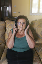 Glückliche ältere Frau, die zu Hause über Kopfhörer Musik hört - EGHF00556