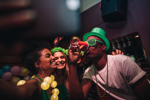 Mann trinkt ein Glas Bier mit weiblichen Freunden lächelnd und nehmen selfie an der Bar. Junge Leute feiern St.Patricks Tag im Nachtclub und nehmen selfie mit Telefon. - JLPSF04914