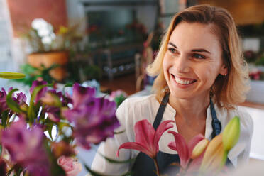 Lächelnde junge Frau, die in einer Gärtnerei für Zimmerpflanzen arbeitet. Glückliche Floristin, die in einem Blumenladen wegschaut und lächelt. - JLPSF04918