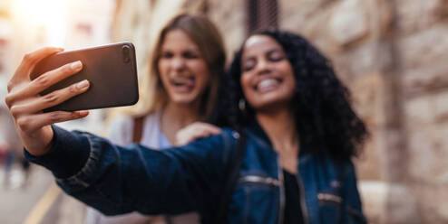 Girls clicking a selfie using mobile phone. Blurred image of women standing outdoors and making faces while posing for a selfie. - JLPSF04920