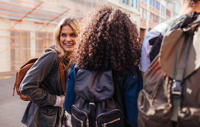 Cheerful woman with friends exploring the city. Young people wearing travel bags moving around in the city. - JLPSF04924