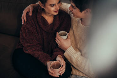 Draufsicht auf ein verliebtes Paar, das mit einem Kaffee zu Hause zusammensitzt. Zärtlicher Mann und Frau zu Hause mit Kaffee. - JLPSF04940