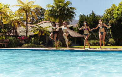 Gruppe von Freundinnen, die in den Swimmingpool springen. Frauen im Bikini, die glücklich aussehen, während sie zusammen in den Swimmingpool springen. - JLPSF04968