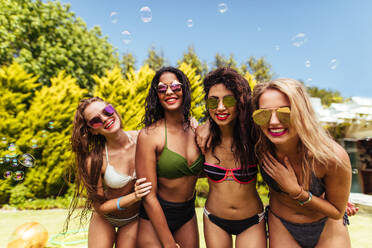 Group of beautiful young woman in bikini looking at camera and smiling. Female friends posing for a photo at the poolside. - JLPSF04978