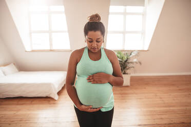 Porträt einer schönen schwangeren Frau, die Yogaübungen macht und ihren Bauch berührt. Schwangere Frau, die zu Hause Yoga übt. - JLPSF05001