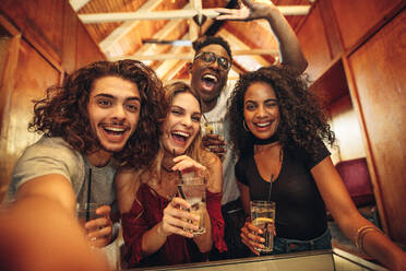 Group of happy young friends with drinks gathered for party in club. Excited men and woman with drinks taking selfie during party. - JLPSF05003