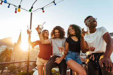 Group of young friends having fun, drinking and enjoying a evening on rooftop. Multiracial men and woman hanging out at rooftop party in evening. - JLPSF05005