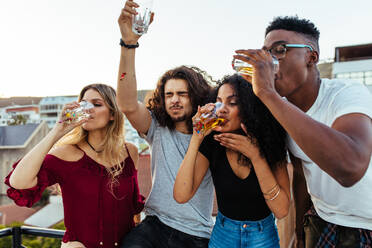 Eine Gruppe junger Freunde trinkt und genießt den Abend auf einer Dachterrasse. Multirassische Männer und Frauen trinken auf einer Dachterrassenparty. - JLPSF05012