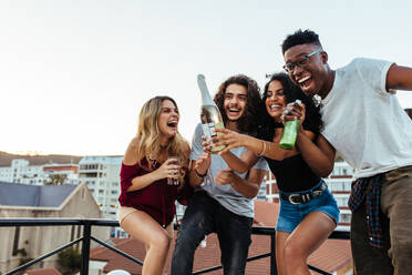 Außenaufnahme einer jungen Frau, die mit Freunden eine Flasche Champagner öffnet. Junge Leute trinken Champagner auf einer Dachterrassenparty. - JLPSF05015