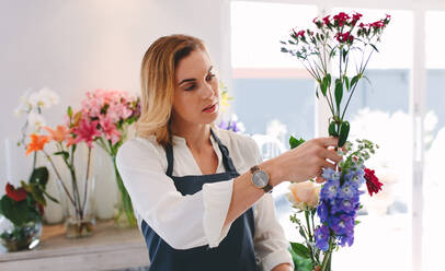 Female working at flower shop arranging flowers. Woman florist making bouquet with various flowers. - JLPSF05043