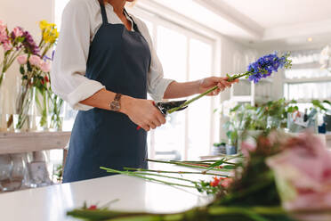 Die Hände einer jungen Floristin, die Blumen mit einer Schere schneidet und einen Blumenstrauß auf dem Ladentisch gestaltet. - JLPSF05050
