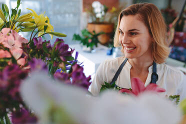 Schöne kaukasische Frau in einem Blumenladen, lächelnde Floristin, die Blumen in ihrem Laden betrachtet. - JLPSF05057