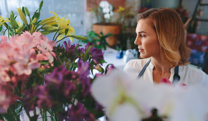 Kaukasische Frau, die in einem Blumenladen arbeitet. Eine Floristin betrachtet Blumen in ihrem Geschäft. - JLPSF05058