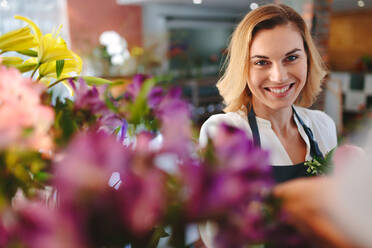 Junge erfolgreiche Kleinunternehmerin Floristin in ihrem eigenen Blumenladen lächelt glücklich. Kaukasische Frau lächelt im Blumenladen. - JLPSF05060