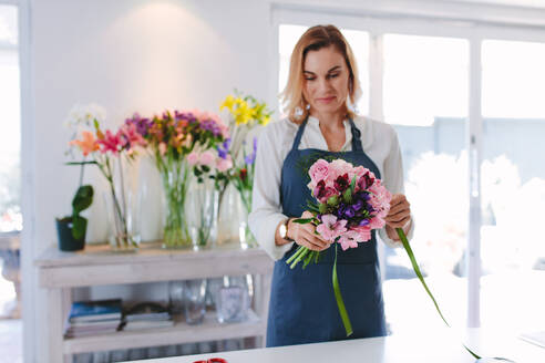 Blumenhändlerin bei der Arbeit, die einen Strauß vorbereitet; Frau steht am Tresen und macht einen Strauß frischer Blumen. - JLPSF05062