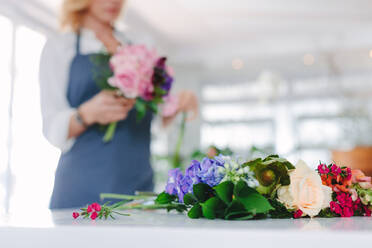 Fresh flower on counter with woman florist working in background. Focus on colorful and fresh flower on florist table. - JLPSF05063