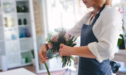 Skillful female florist creating bouquet of flowers. Young woman florist arranging flowers at workshop. - JLPSF05065