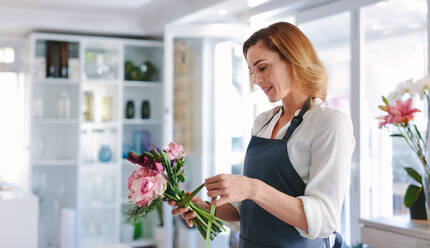 Frau Floristin bereitet einen Blumenstrauß in ihrem Geschäft vor. Frau arbeitet in einem Blumenladen und macht einen Strauß mit frischen Blumen. - JLPSF05066