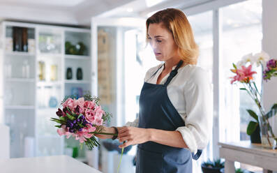 Floristin, die in einem Geschäft einen Blumenstrauß zusammenstellt; Floristin, die in einer Werkstatt einen Blumenstrauß arrangiert und gestaltet. - JLPSF05067