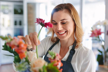 Female florist arranging flowers. Woman flower shop owner placing flowers in a bouquet. - JLPSF05071