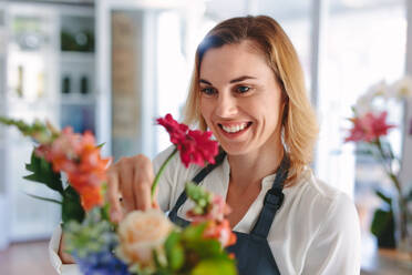 Lächelnde Floristin, die einen Blumenstrauß zubereitet. Frau, die einen Strauß frischer Blumen im Einzelhandelsgeschäft zubereitet. - JLPSF05072