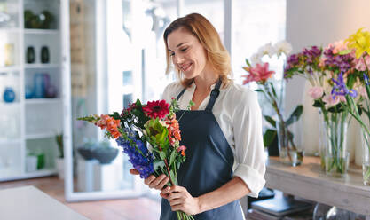 Glückliche Floristin, die in ihrem Geschäft einen Blumenstrauß herstellt. Floristin mit einem Blumenstrauß in der Werkstatt. - JLPSF05073