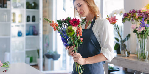 Frau arbeitet in einer Gärtnerei für Zimmerpflanzen. Glückliche Floristin mit einem Blumenstrauß in der Hand in ihrem Blumenladen. - JLPSF05074