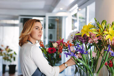 Floristin in einem Blumenladen, die frische Blumen in einer Vase arrangiert. Junge Frau arbeitet in einem Blumenladen. - JLPSF05076