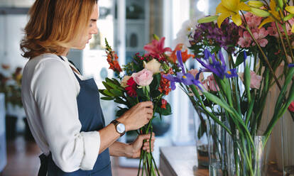 Frau Floristin bereitet einen Strauß mit frischen Blumen in ihrem Geschäft vor. Frau arbeitet in einem Blumenladen und macht einen Strauß. - JLPSF05078
