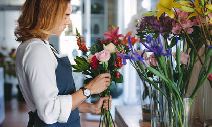 Woman florist preparing a bouquet with fresh flowers at her shop. Woman working at flower shop making bouquet. - JLPSF05078