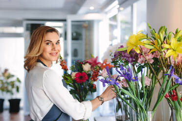 Glückliche Floristin, die in ihrem Geschäft einen Blumenstrauß herstellt. Frau, die in einem Blumenladen einen Blumenstrauß herstellt. - JLPSF05079