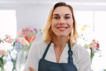 Close up of young successful florist standing in her own flower shop. Smiling flower shop worker looking at camera. - JLPSF05083