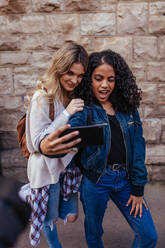 Cheerful girls taking a selfie using mobile phone. Women standing outdoors and making faces while posing for a selfie. - JLPSF05097