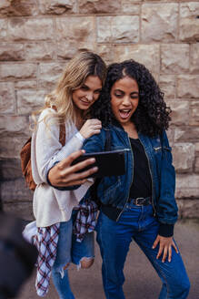 Fröhliche Mädchen, die ein Selfie mit dem Handy machen. Frauen, die im Freien stehen und Gesichter machen, während sie für ein Selfie posieren. - JLPSF05097