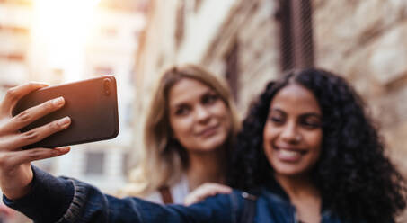 Girls clicking a selfie using mobile phone. Blurred image of women standing outdoors and posing for a selfie. - JLPSF05098