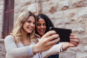 Fröhliche Mädchen machen ein Selfie mit dem Handy. Frauen stehen im Freien und lächeln, während sie für ein Selfie posieren. - JLPSF05099